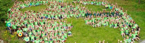Viele naturbegeisterte Kinder mit grünene T-Shirts sitzen im Kreis und bilden gemeinsma das Logo des Nationalparks Sächsishce Schweiz ab.