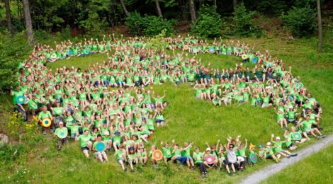 Viele naturbegeisterte Kinder mit grünene T-Shirts sitzen im Kreis und bilden gemeinsma das Logo des Nationalparks Sächsishce Schweiz ab.